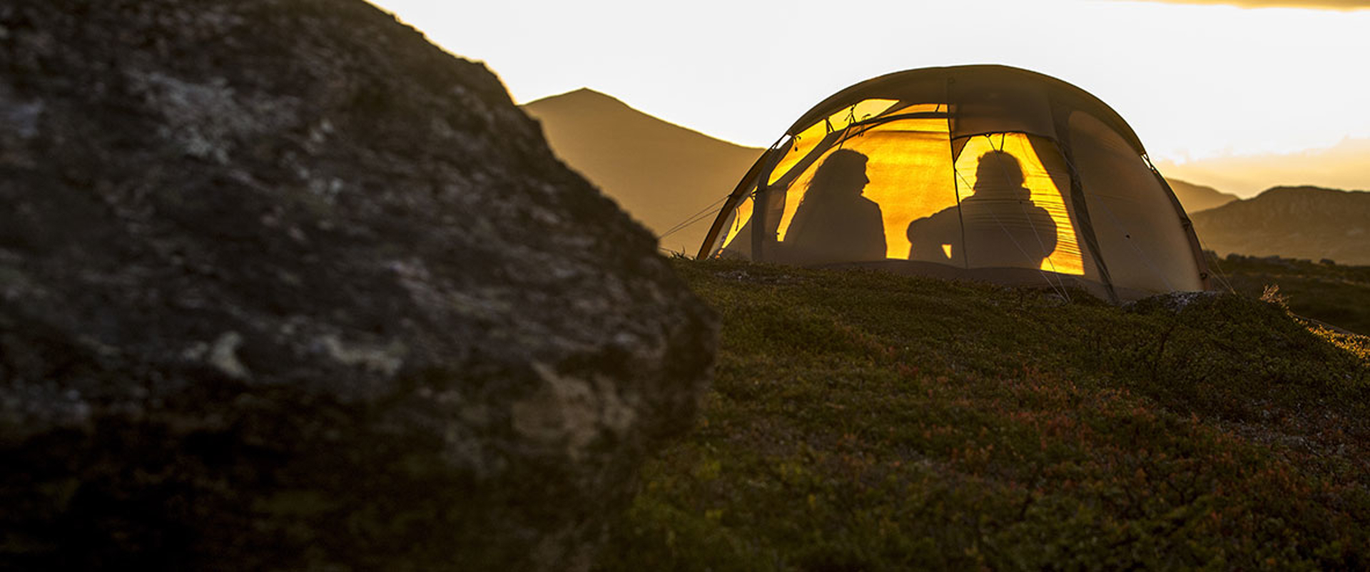 Silhouette of two people inside a tent at sunset