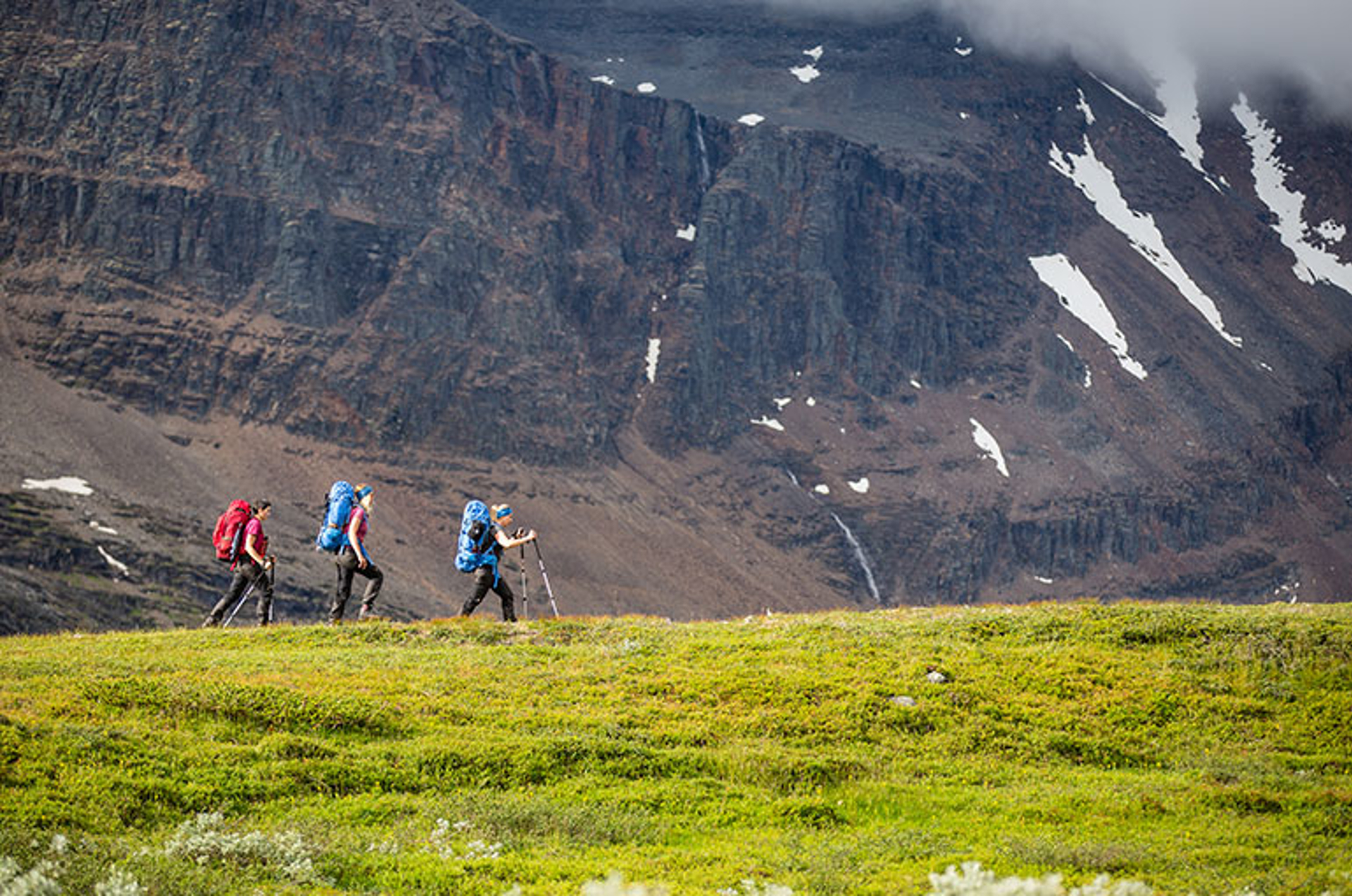 Three people hiking in front of large mountain
